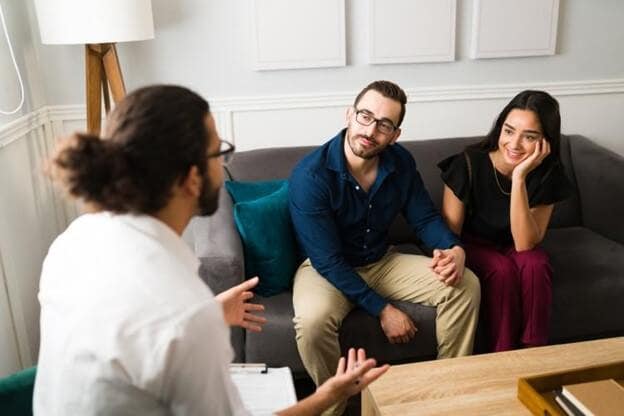 A couple seated on a couch listens to a marriage counselor.