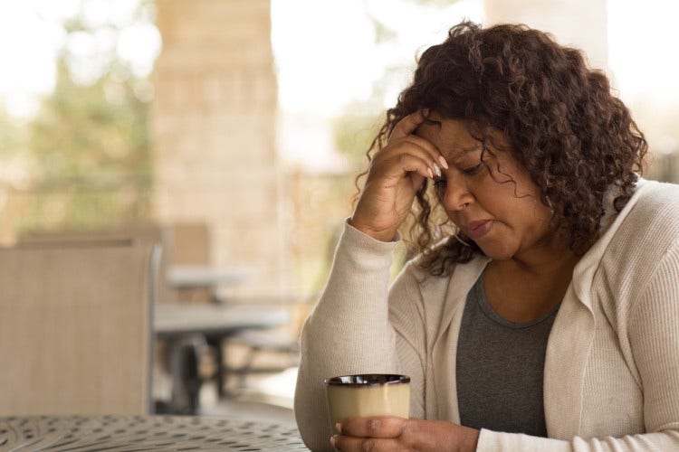 A depressed woman sitting alone at a table, holding a mug.