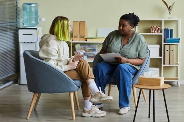A substance abuse counselor holding a clipboard meets with a young client.