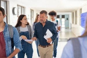 A high school counselor speaks with a student while they walk down a school hallway together.