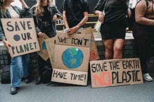 Climate change demonstrators holding cardboard signs reading “Save our planet,” “We don’t have time!” and “Save the Earth no plastic.”