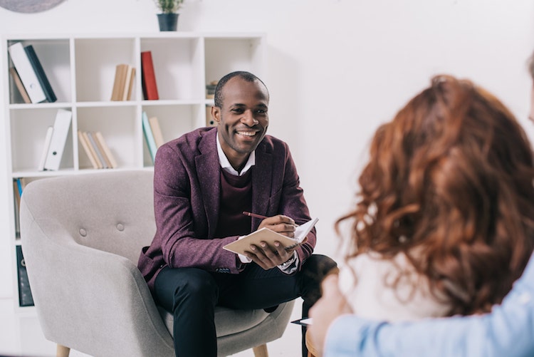 A counselor takes notes on a notepad while meeting with a client.